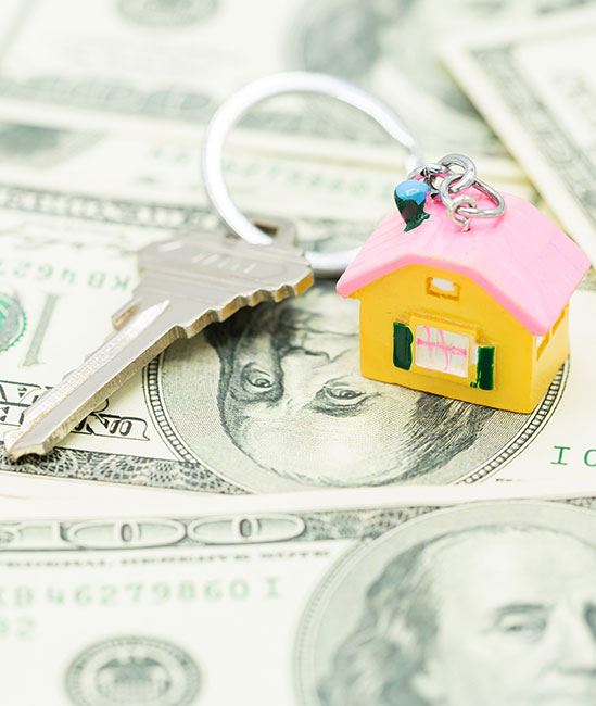 Photo of house key ring with silver tone key on top of $100 bank notes.